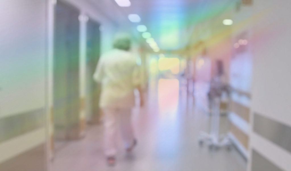 Sjukepleiar i ein sjukehuskorridor. Bildet har regnbogefilter.