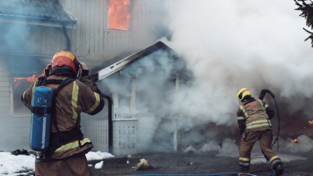 To brannkonstabler er i gang med å slukke brann i et hus.