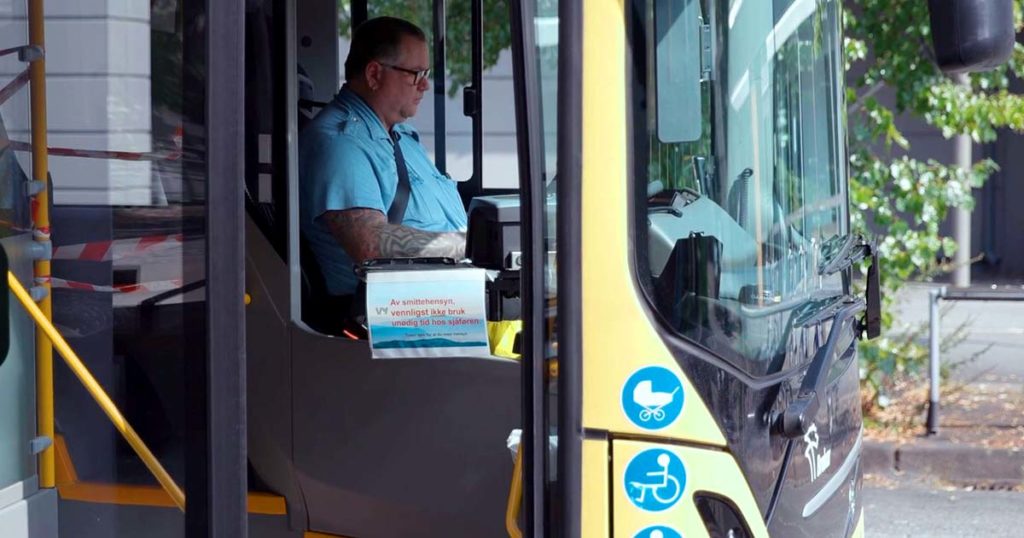 Bussjåfør bak rattet i ein buss ved ein haldeplass.