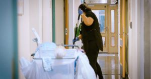 Reinholder med vasketralle vasker gulv i en korridor, med en mopp.