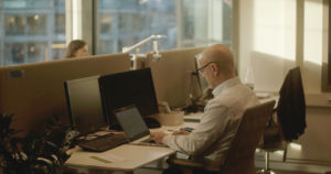 To personer arbeider i et kontorlandskap, på hver sin side av en skillevegg