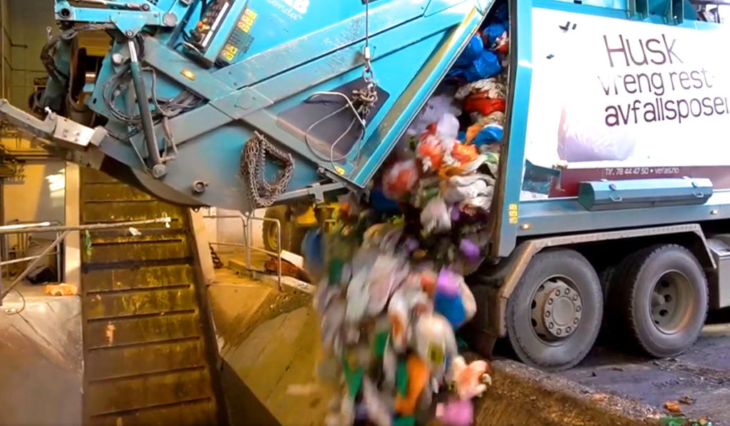 Avfallsbil tømmer avfallsposer i sjakt i avfallsanlegg