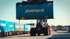 Ein stor truck løftar ein transportkontainer på ein godssentral.