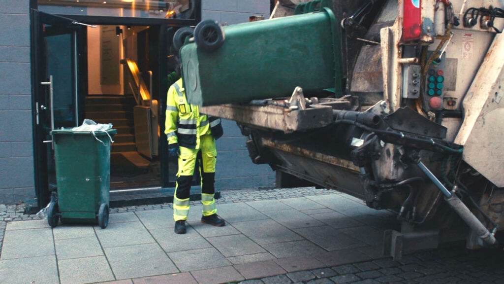 En renovatør tømmer en avfallscontainer i en avfallsbil
