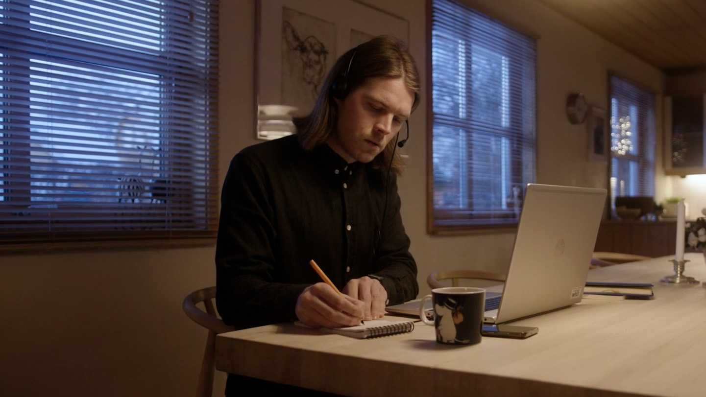 Mann ved spisebord arbeider med bærbar PC, notatblokk og kaffekopp.