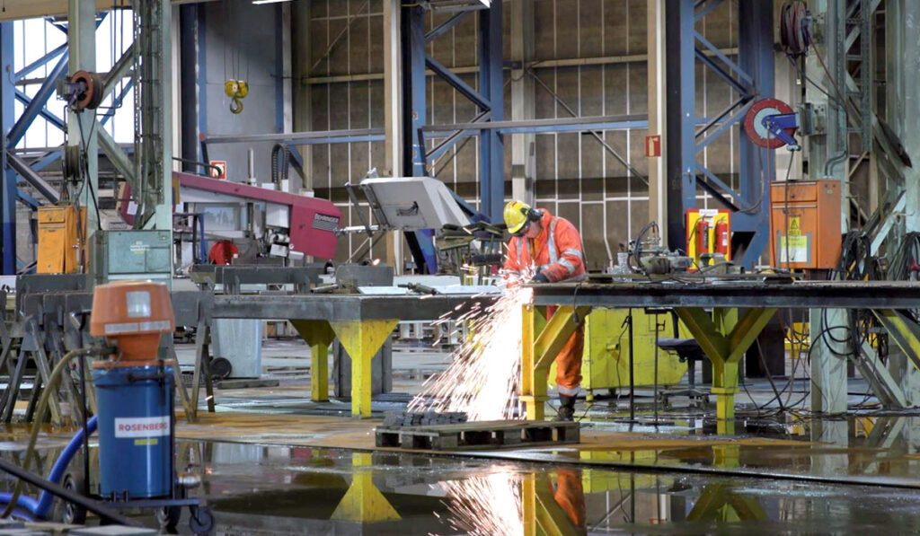 Operatør i en industrihall skjærer i stål med en vinkelsliper.