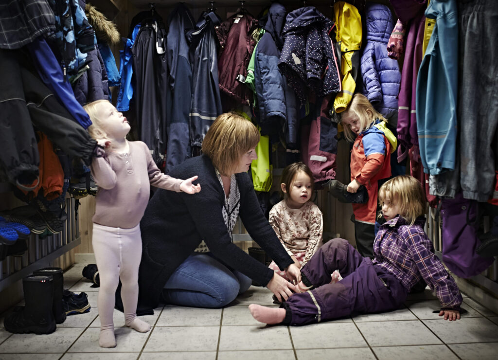 Kvinnelig barnehageansatt sitter på gulvet med barn i gardertoben.