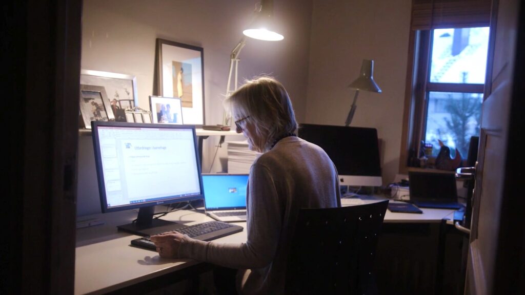 Kvinne arbeider ved PC-skjerm på et hjemmekontor i eget rom i en privatbolig.