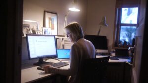 Kvinne arbeider ved PC-skjerm på et hjemmekontor i eget rom i en privatbolig.