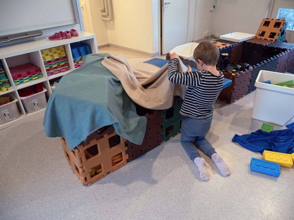 Gutt sett bakfra mens han leker med kasser og tepper.