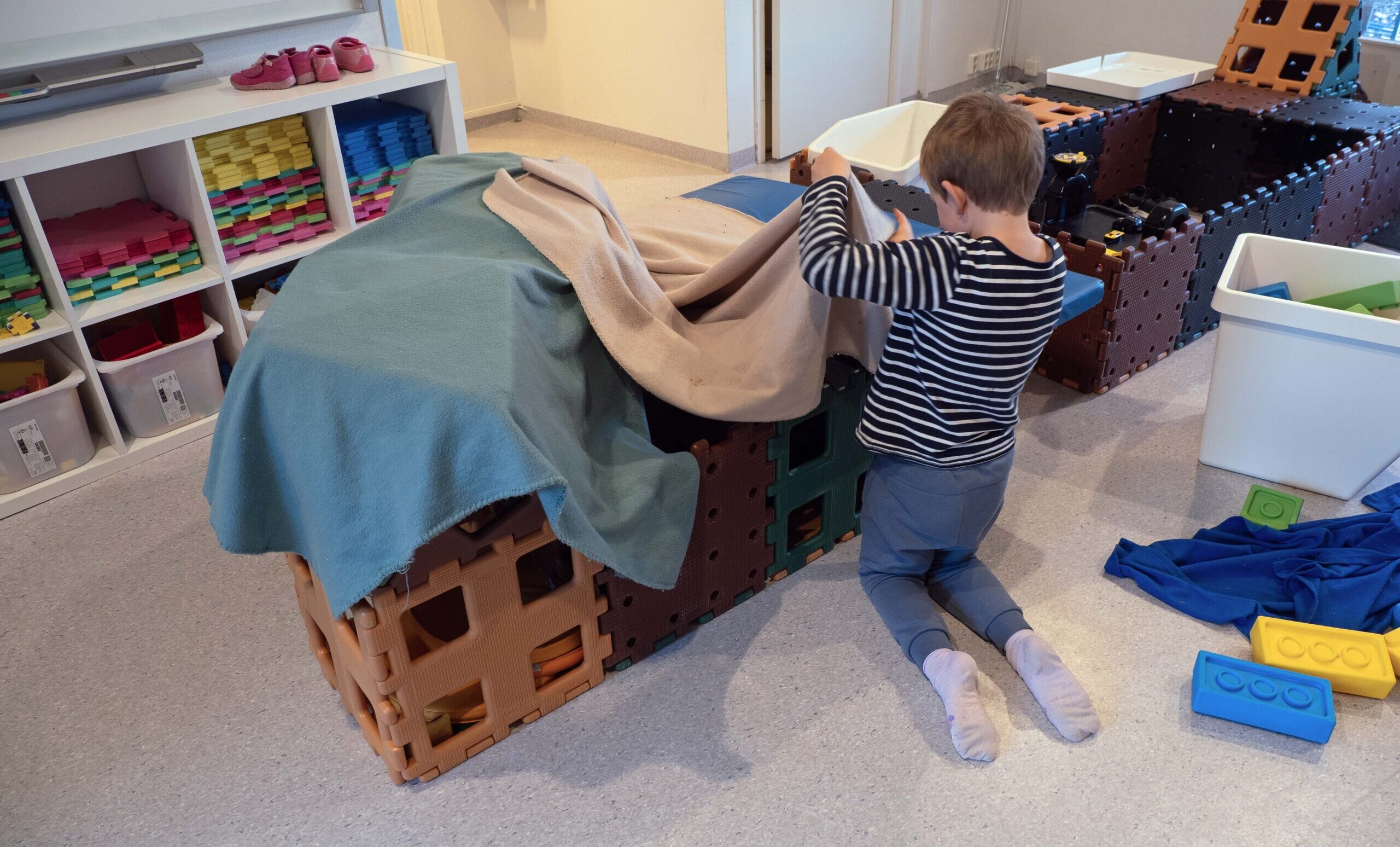 Gutt sett bakfra mens han leker med kasser og tepper.