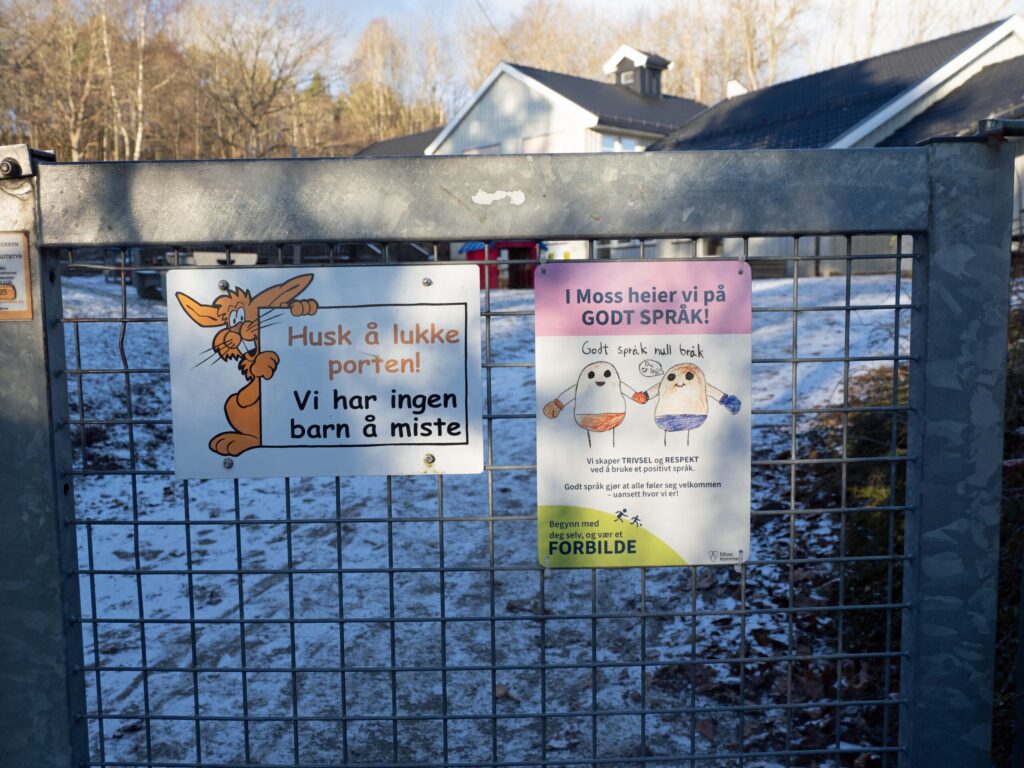 Banrhage sett utenfra. Snå på bakken og to plakater på grinden.