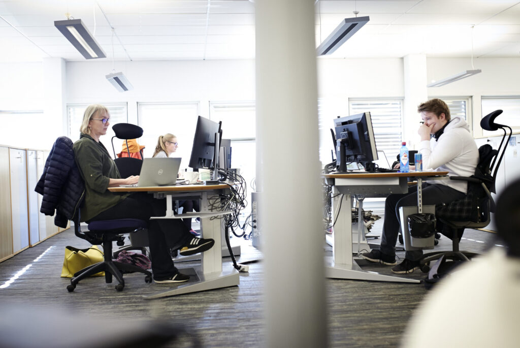 To personar arbeider framfor skjermar i eit kontorlandskap