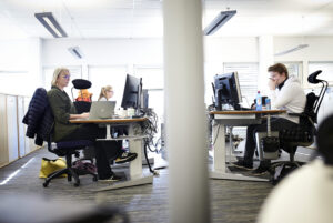 To personar arbeider framfor skjermar i eit kontorlandskap