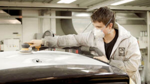 Bilmekaniker med støvmaske sliper en overflate på en bil