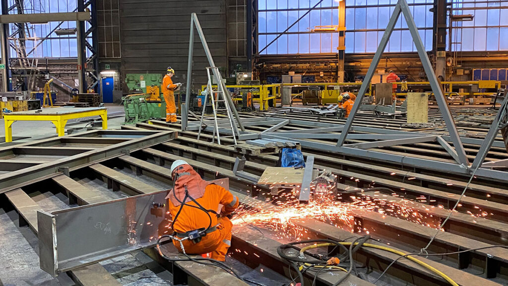 Person med verneutstyr kutter stål på ein stålkonstruksjon i eit produksjonslokale
