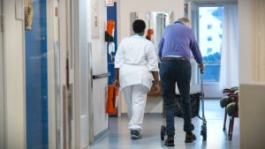 Ein tilsett på sjukeheim går i ein korridor saman med ein bebuar som går med rullator.