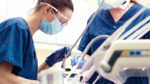 Tannhelsepersonell med briller og munnbind står over ein pasient