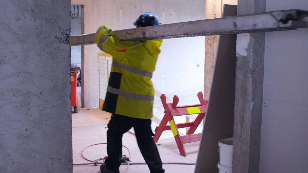 Handverker bærer et stillaselement på en byggeplass