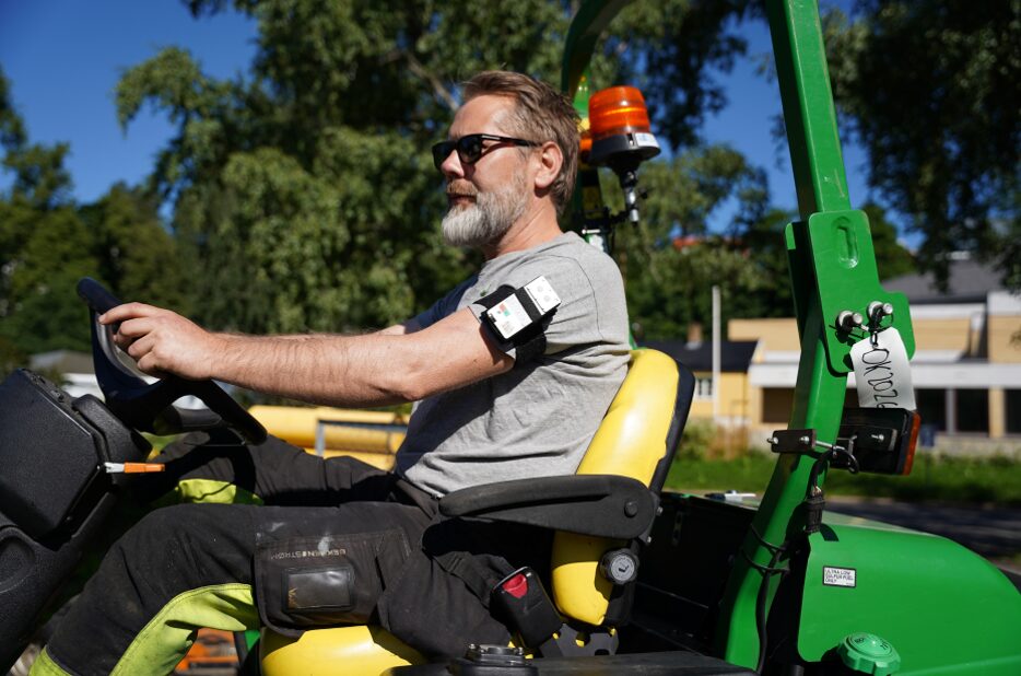 Mann i traktor, i solen med måleutstyr på armen.