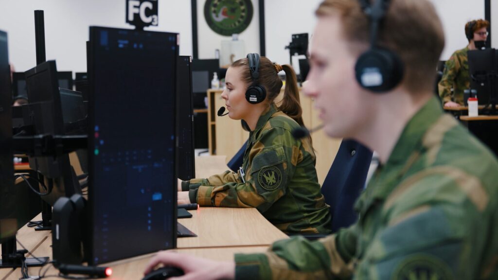 To uniformerte personer arbeider foran PC-skjermer, et kontorlokale