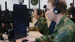 To uniformerte personer arbeider foran PC-skjermer, et kontorlokale