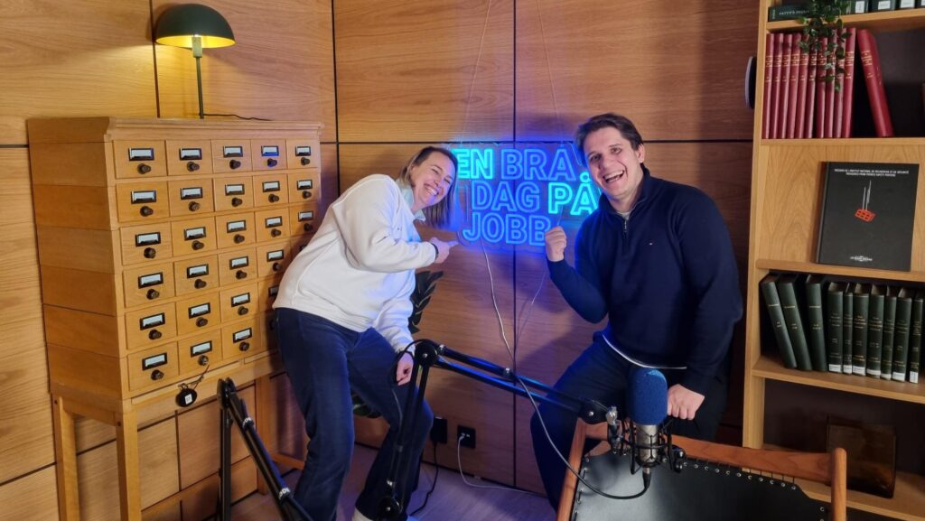 Anne-Mette Aasheim fra Fornybar Norge sammen med programleder Daniel Kolbeinshavn. Peker fornøyd mot et lysende skilt hvor det står "En bra dag på jobb".