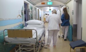 To sjukepleiarar i ein sjukehusgang flyttar ei seng og eit stativ