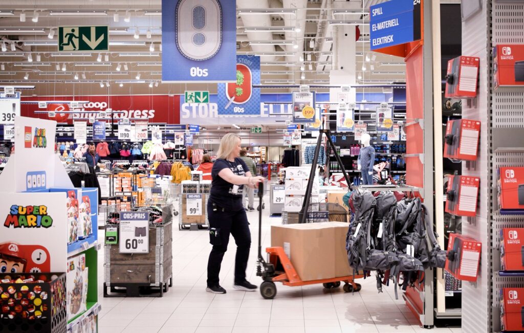 Butikkansatt dytter en tralle med vare remllom fulle hyller.