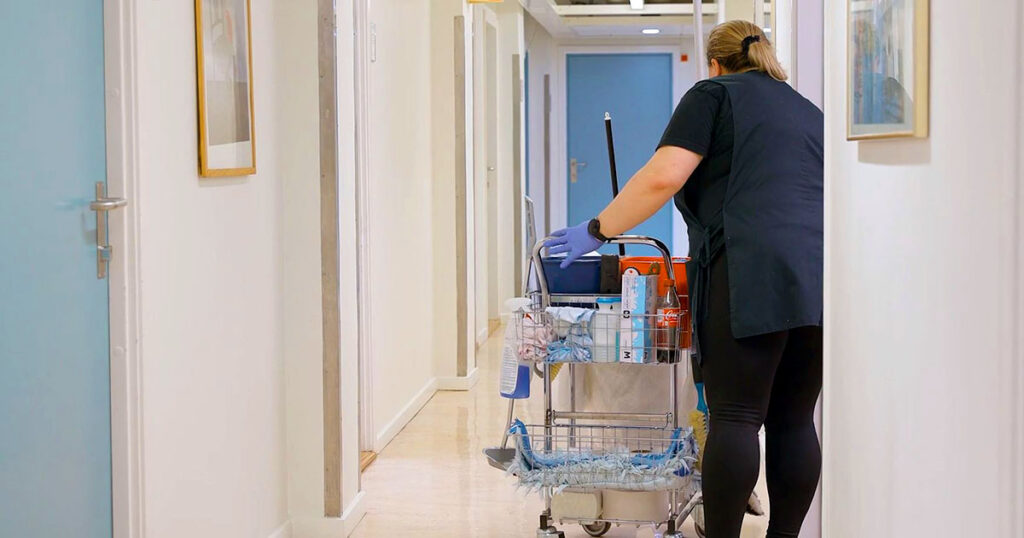 Renholder med en utstyrstralle i en korridor